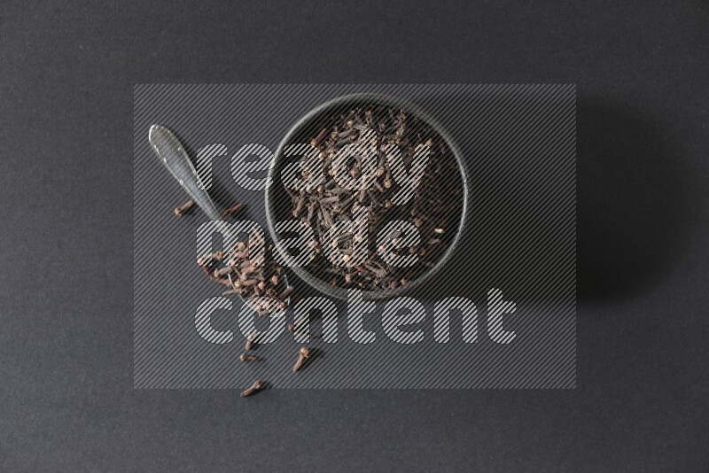 وعاء فخاري أسود ممتلئ بحبوب القرنفل مع ملعقة معدنية بجانبه علي خلفية سوداء