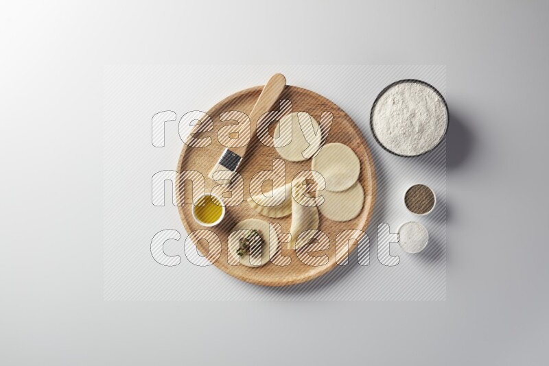 two closed sambosas and one open sambosa filled with meat while flour, salt, black pepper and oil with oil brush aside in a wooden dish on a white background