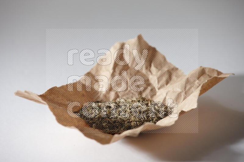 Cumin seeds in a crumpled piece of paper on white flooring