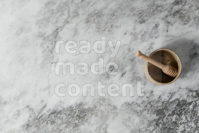 Multicolored pottery bowl with wooden honey dipper in it on grey marble background