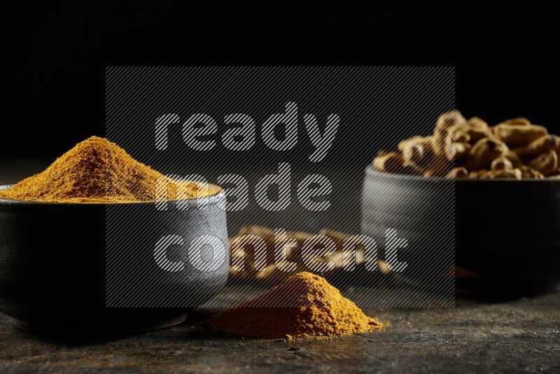 وعاءان من الفخار باللون الأسود، أحدهما ممتلئ ببودرة الكركم والآخر ممتلئ بأصابع كاملة من الكركم المجفف على خلفية سوداء