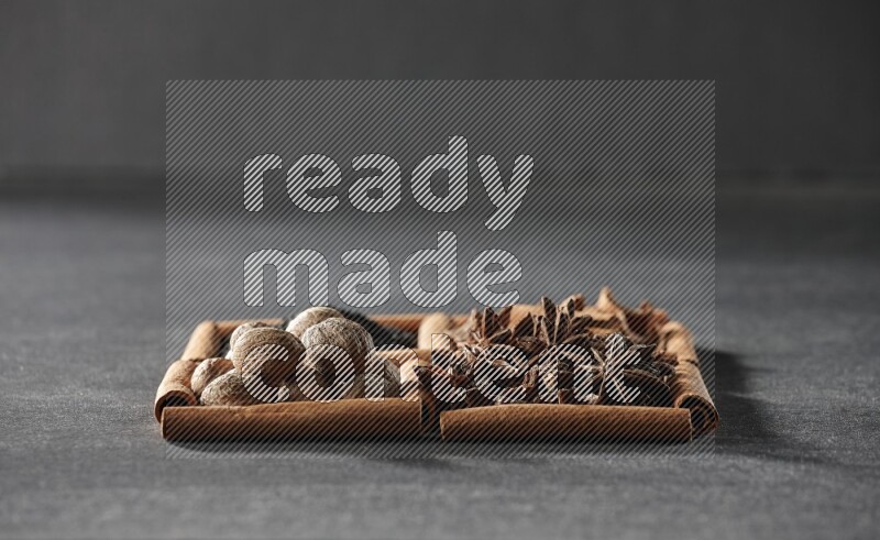 4 squares of cinnamon sticks full of black seeds, cinnamon, star anise and nutmegs on black flooring