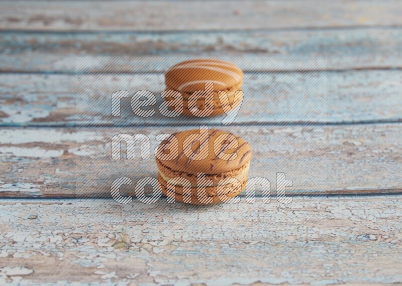 45º Shot of of two assorted Brown Irish Cream, and light brown Almond Cream macarons next to each other on light blue background