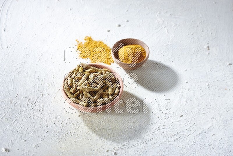 2 wooden bowls, one full of turmeric powder and the other full of dried turmeric whole fingers on a textured white flooring