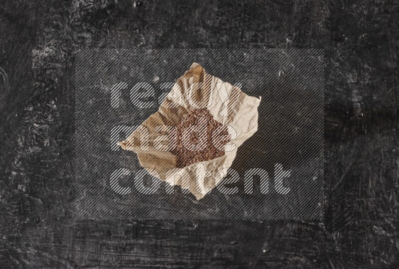 A crumpled piece of paper full of flaxseeds on a textured black flooring