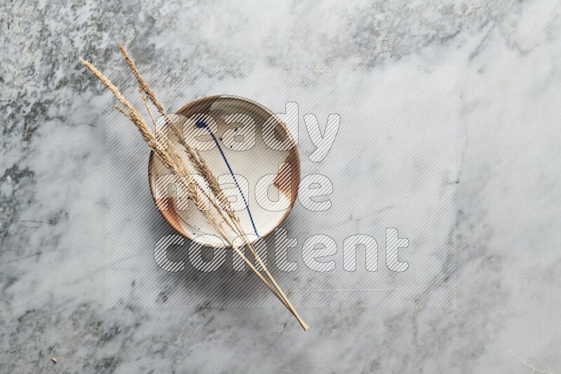 Wheat stalks on multicolored pottery plate on grey marble background
