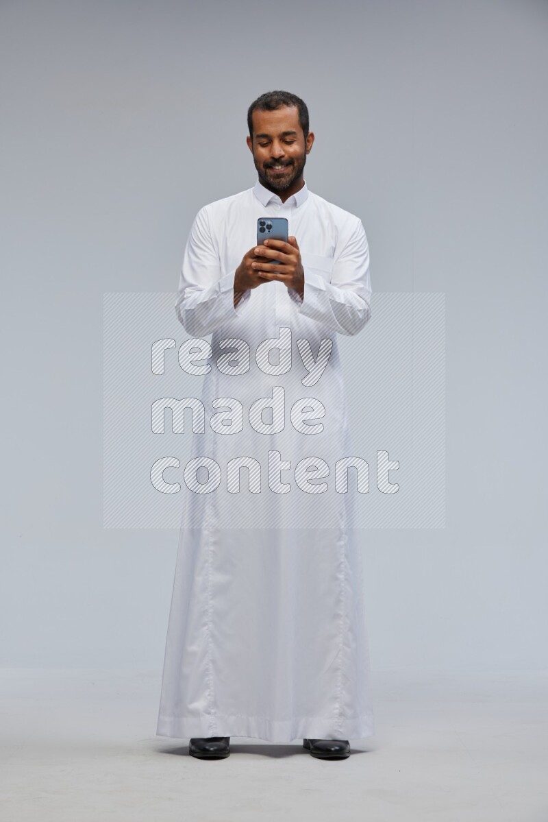 Saudi man wearing Thob standing texting on phone on Gray background
