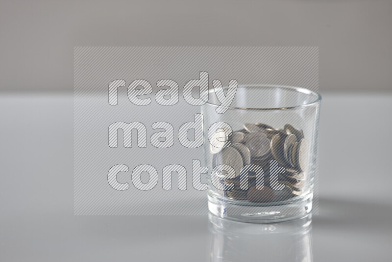 Random old coins in a glass cup on grey background