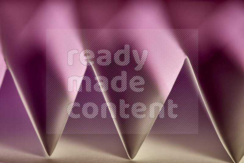 A close-up abstract image showing sharp geometric paper folds in pink gradients and warm tones