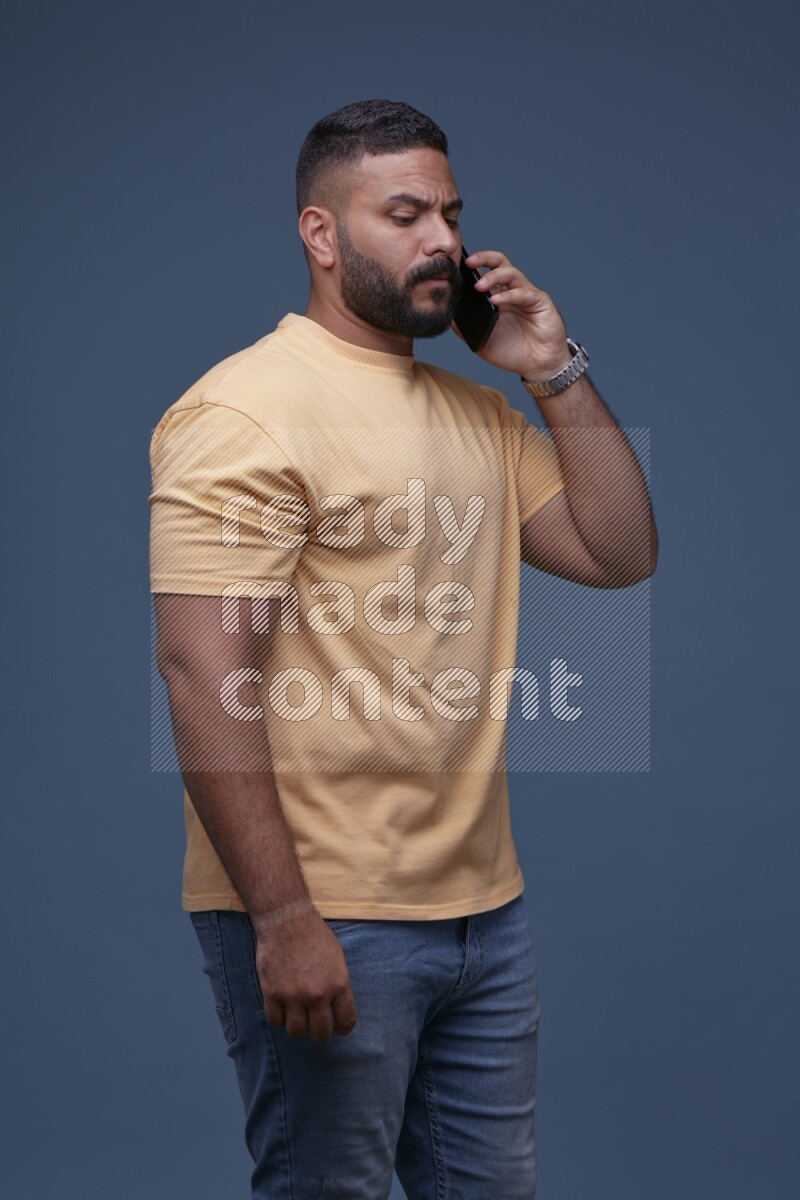 رجل يرتدي بنطال ازرق جينز وقميص اصفر بأكمام قصيره يتحدث بجواله