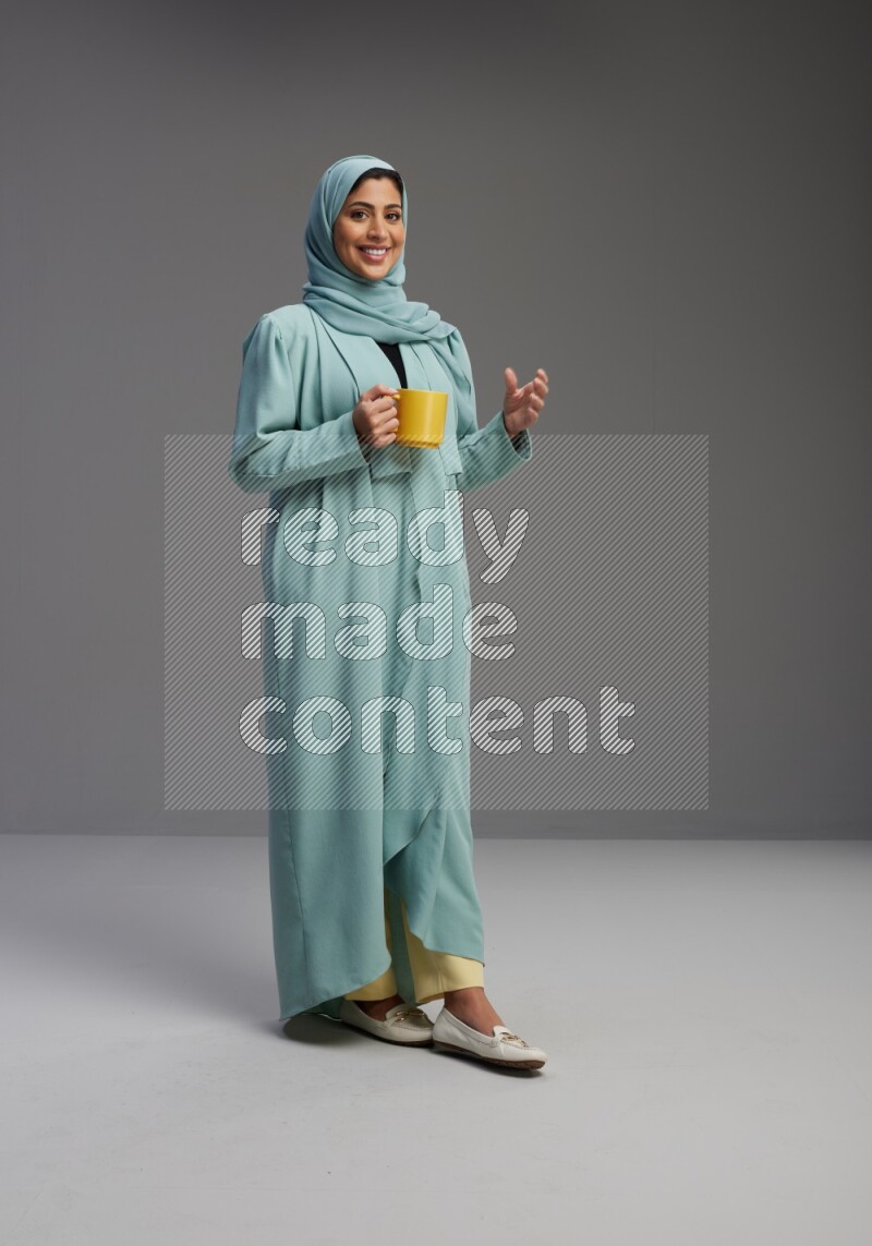 Saudi Woman wearing Abaya standing  holding a mug on Gray background