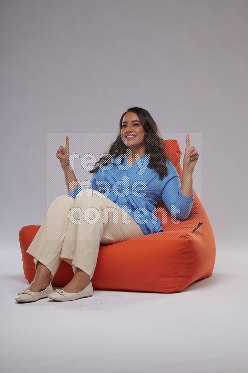 A woman sitting on an orange beanbag and interacting with the camera