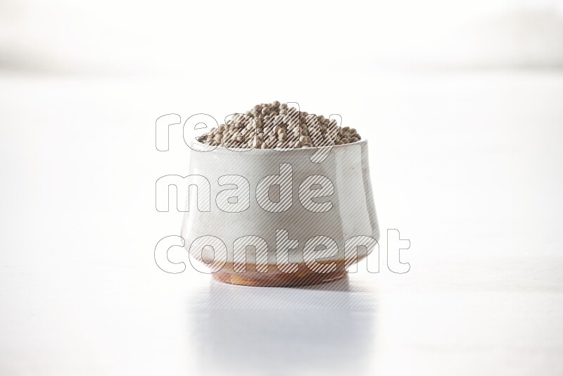 A beige pottery bowl full of white pepper beads on white flooring