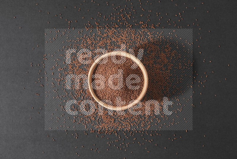 A wooden bowl full of garden cress seeds surrounded by seeds on a black flooring