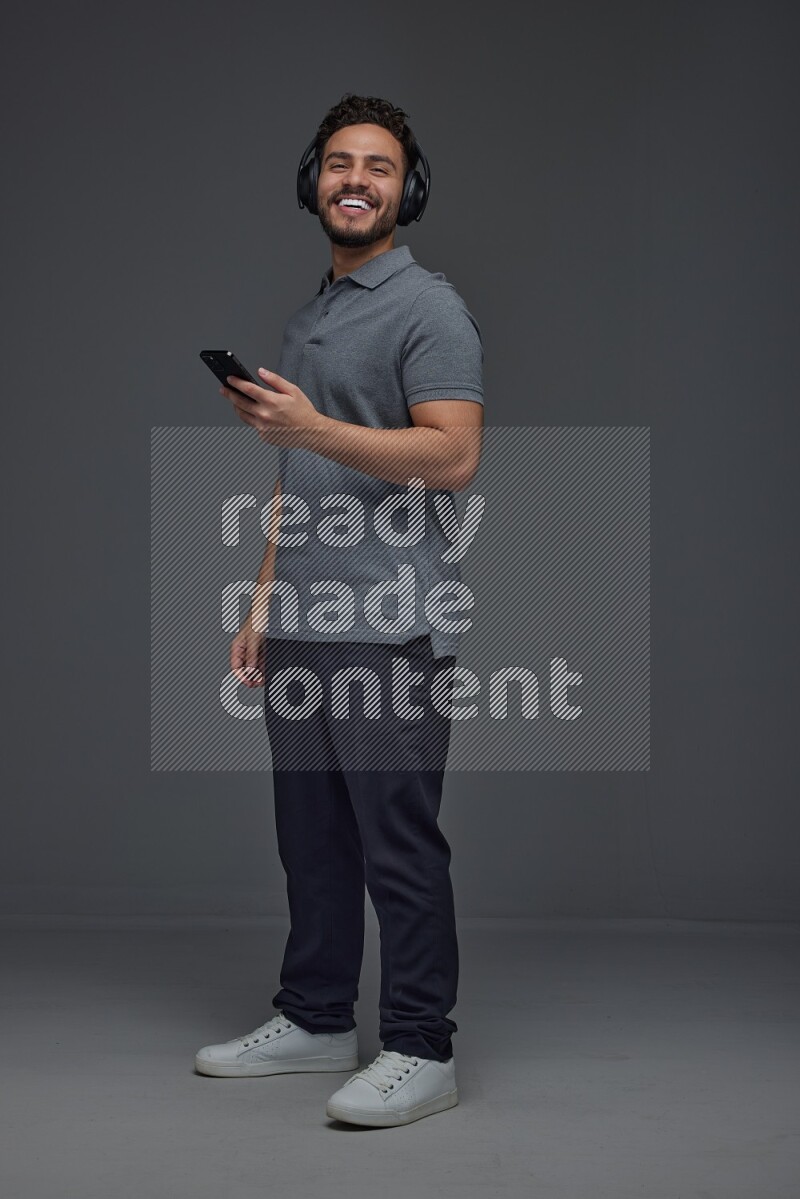 A man wearing casual and using his phone and headphone eye level on a gray background