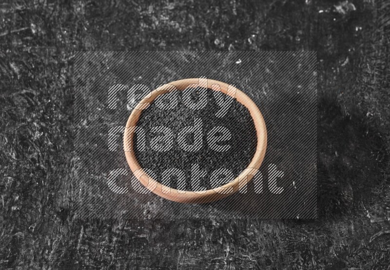 وعاء خشبي ممتلئ ببذور حبة البركة علي خلفية سوداء