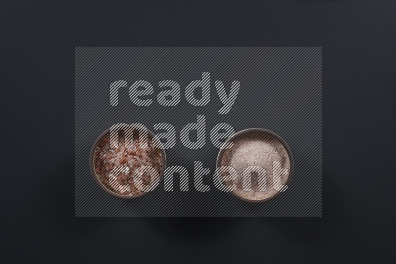 Pottery bowl full of fine himalayan salt and coarse himalayan salt on black background