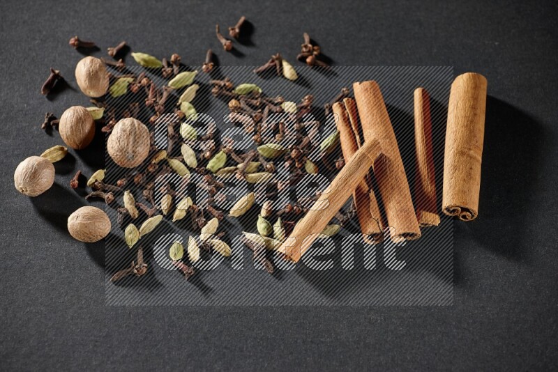 Cardamom, cloves, nutmeg and cinnamon sticks on black flooring