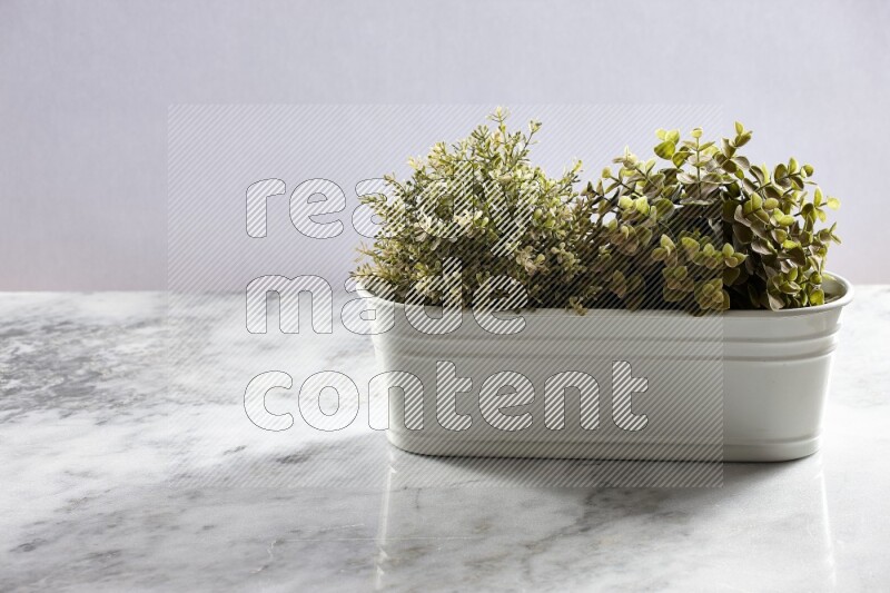 Multiple green artificial plants in white pot on grey marble background