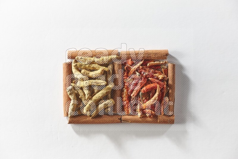 مربعان من أعواد القرفة ممتلئان بالفلفل الحار المجفف وأصابع الكركم علي خلفية بيضاء