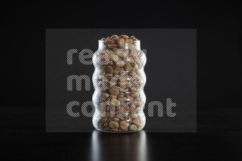 Fava beans in a glass jar on black background