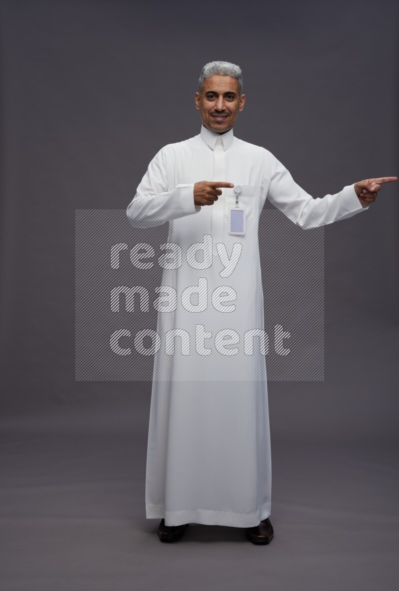 Saudi man wearing thob with pocket employee badge standing interacting with the camera on gray background