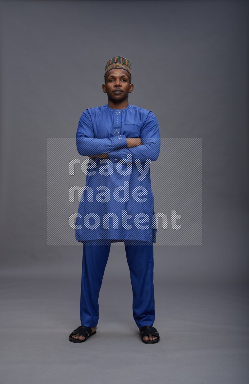 Man wearing Nigerian outfit standing with crossed arms on gray background