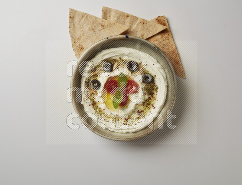 Lebnah garnished with cherry tomato, mint, olives & pine nuts in a grey pottery plate on a white background