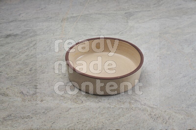 A beige pottery oven bowl on grey marble background