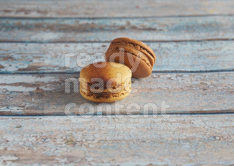 45º Shot of of two assorted Brown Irish Cream, and Yellow Crème Brulée macarons on light blue background