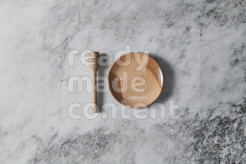 Multicolored pottery plate with wooden honey dipper on the side on grey marble background