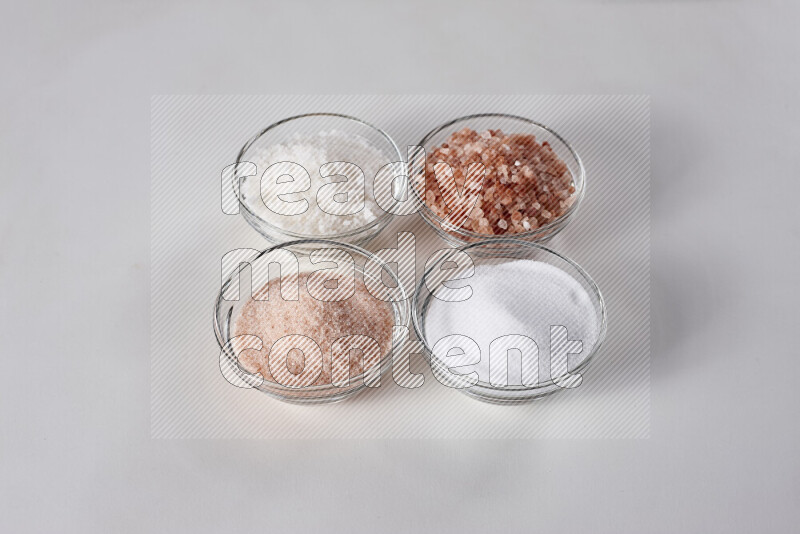 4 glass bowls filled with table salt, coarse sea salt, fine himalayan salt and coarse himalayan salt on white background