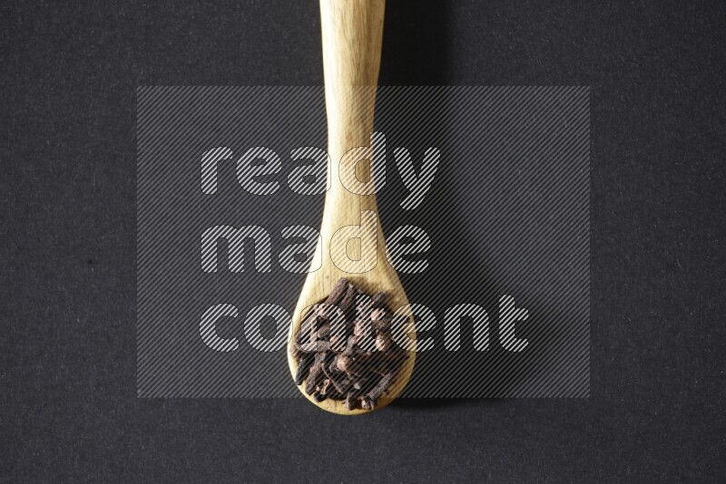 A wooden spoon full of cloves on a black flooring