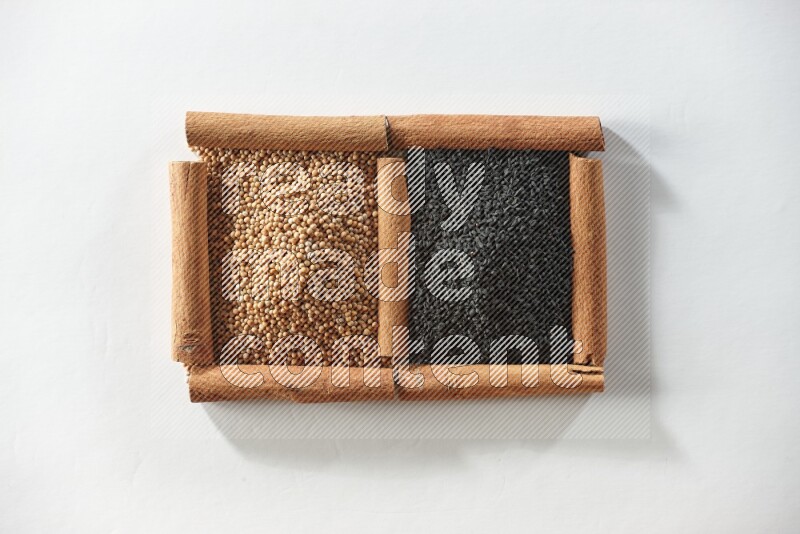 مربعان من أعواد القرفة ممتلئان بحبوب الخردل وحبة البركة السوداء علي خلفية بيضاء