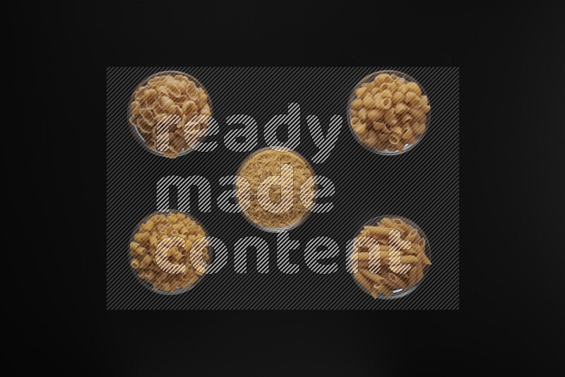 Different pasta types in 5 glass bowls on black background