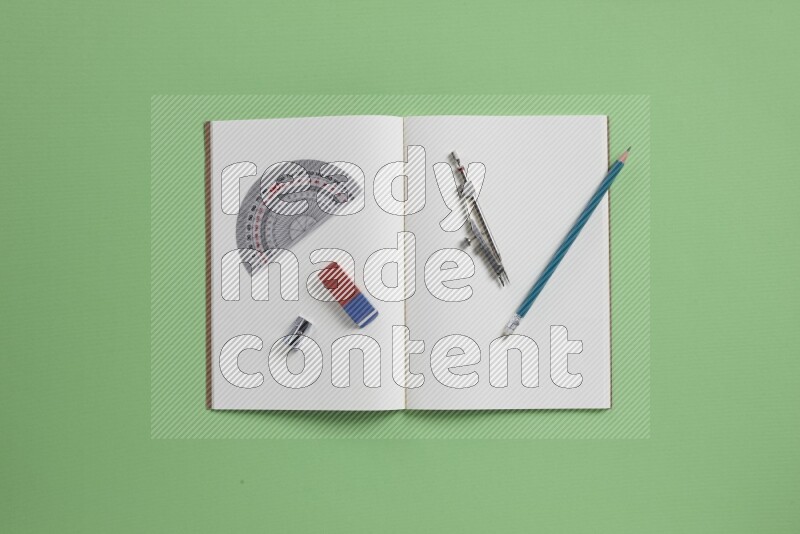 A blank open notebook with different school supplies on green background