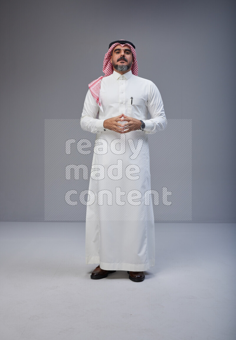 Saudi man Wearing Thob and red white Shomag standing interacting with the camera on Gray background
