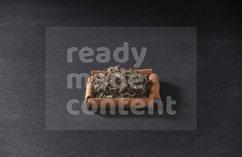 أربعة من أعواد القرفة مكونة شكل مربع بداخلها ريحان مجفف علي خلفية سوداء