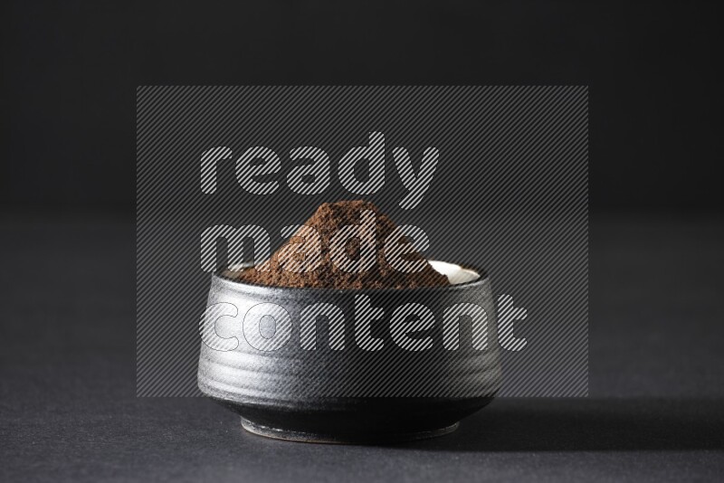 A black pottery bowl full of cloves powder on a black flooring