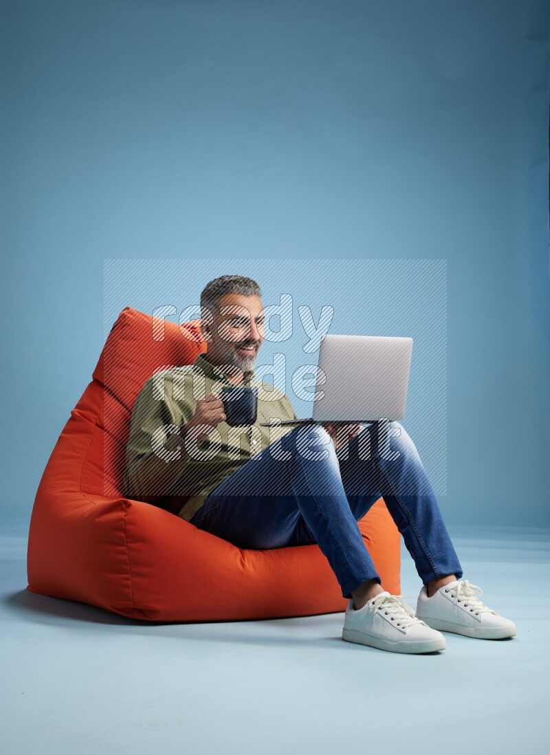 A man sitting on an orange beanbag and working on laptop