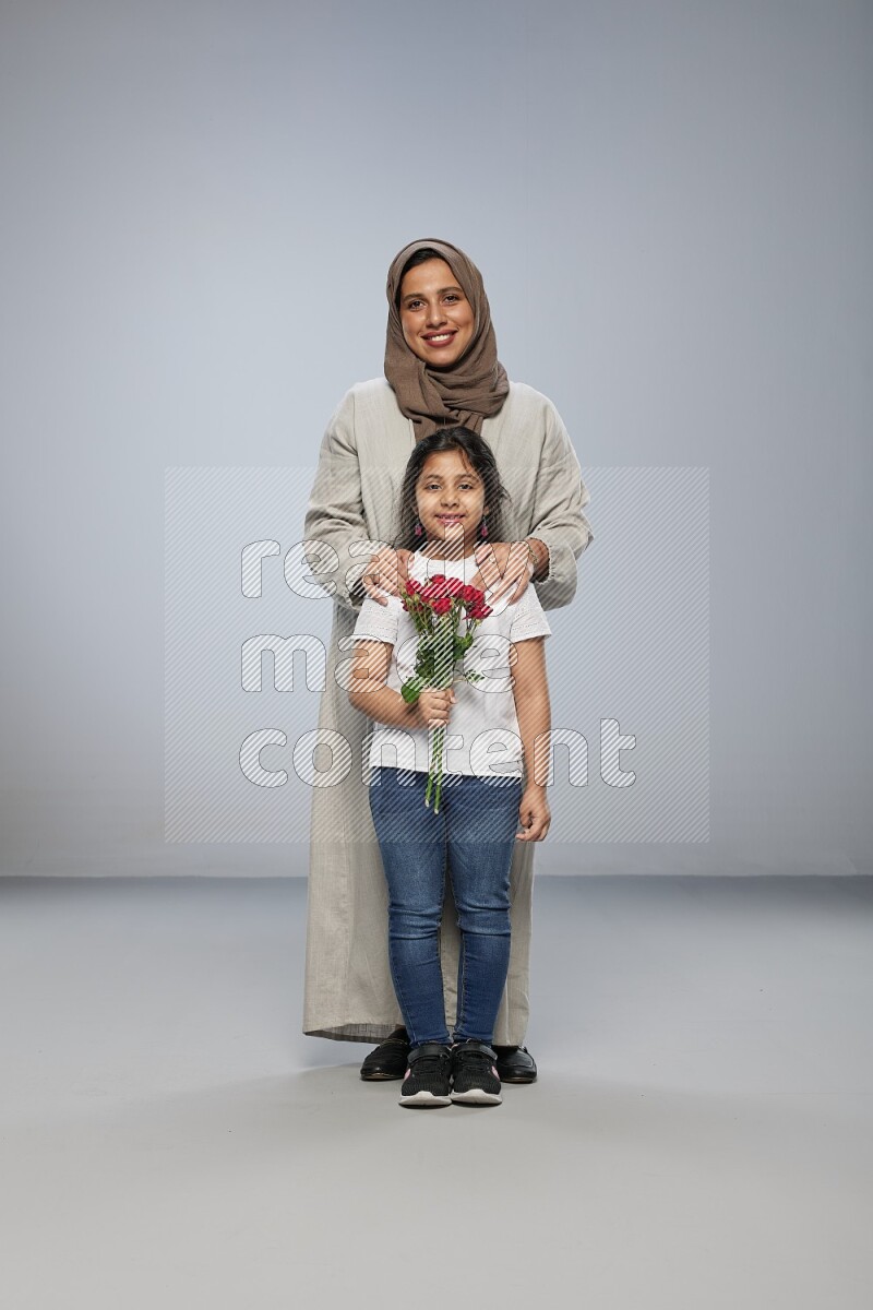 A girl standing giving flowers to her mother on gray background