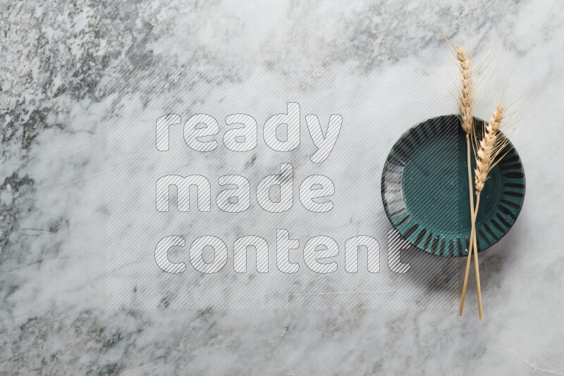 Wheat stalks on multicolored pottery plate on grey marble background