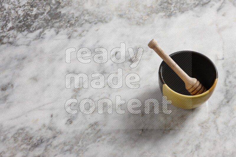 Multicolored pottery bowl with wooden honey dipper in it on grey marble background