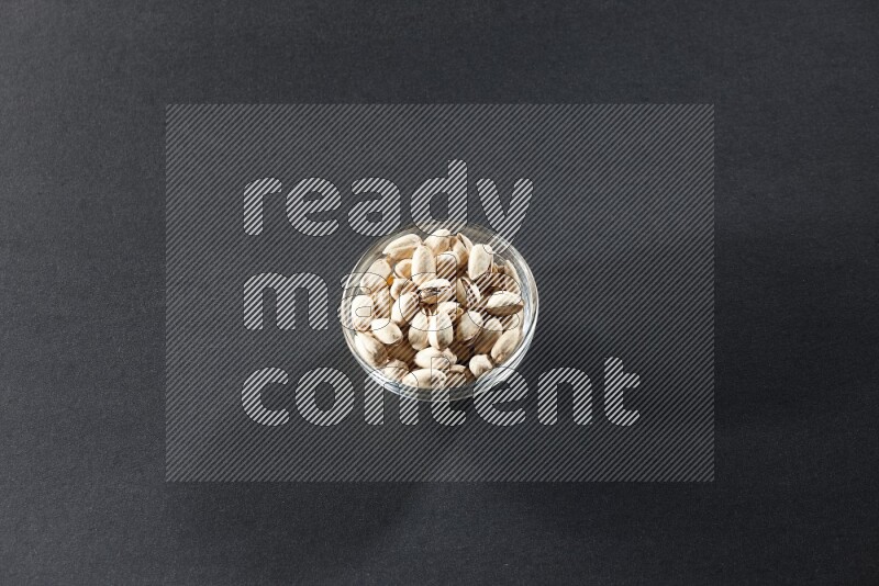 A glass bowl full of pistachios on a black background in different angles