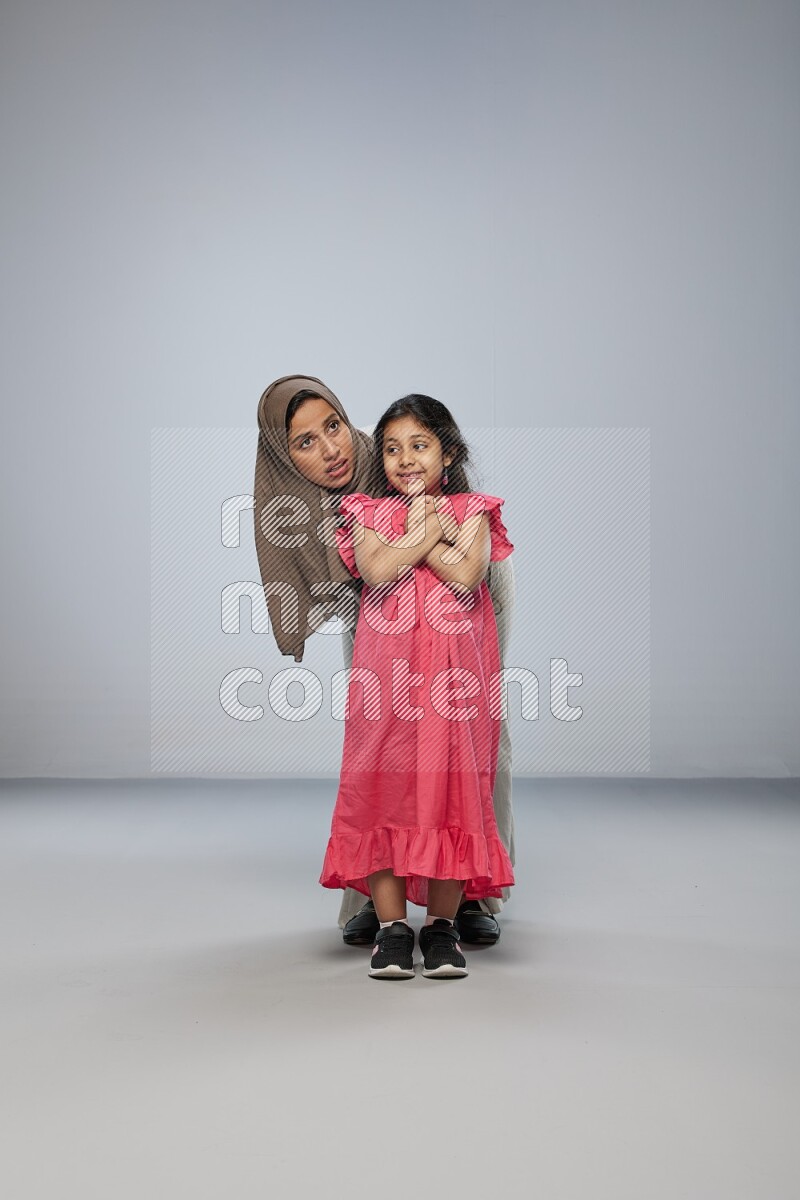 A girl and her mother interacting with the camera on gray background