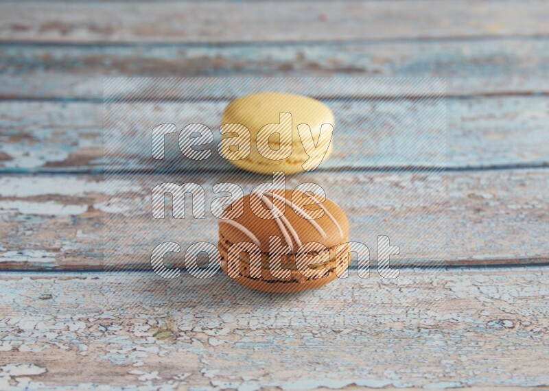 45º Shot of of two assorted Brown Irish Cream, and Yellow Vanilla macarons on light blue background