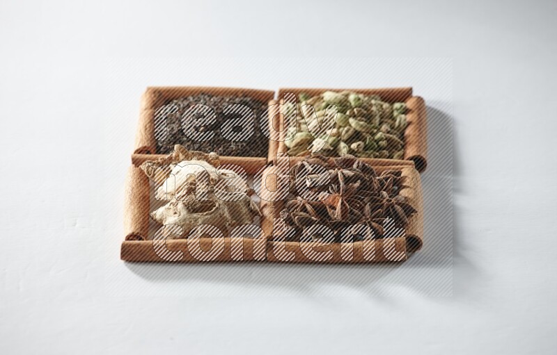 4 مربعات من أعواد القرفة ممتلئة بالشاي والهيل واليانسون والزنجبيل على أرضية بيضاء