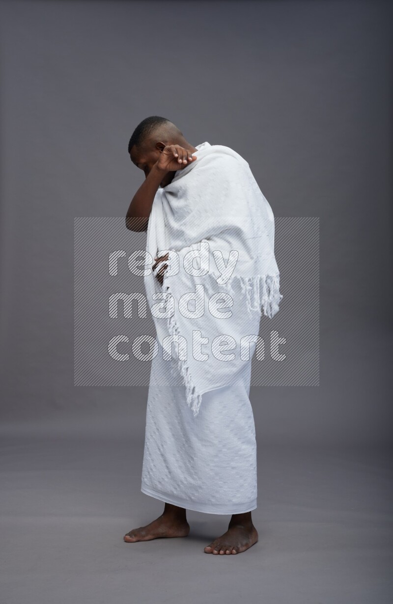 A man wearing Ehram standing showing how to sneeze on gray background