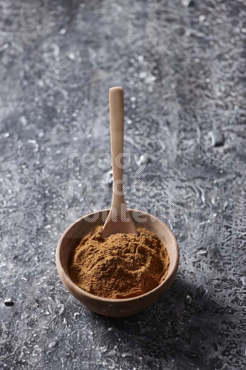 Wooden bowl full of cinnamon powder with a wooden spoon on a textured black background in different angles