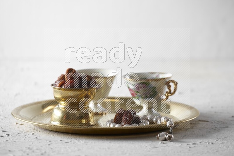 Dates in a metal bowl with tea and prayer beads on a tray in a light setup
